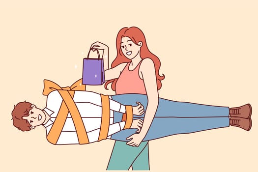 Woman holds man wrapped in gift ribbon as metaphor for romantic valentine day or relationship anniversary gift. Girl with smile shows shopping bag and boyfriend to advertise sale for valentine day