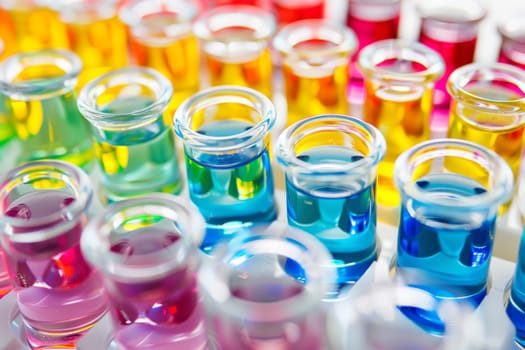 Several vibrant liquids, each in a different color, are neatly arranged in a straight row. The containers holding the liquids are transparent, showcasing their hues and textures.