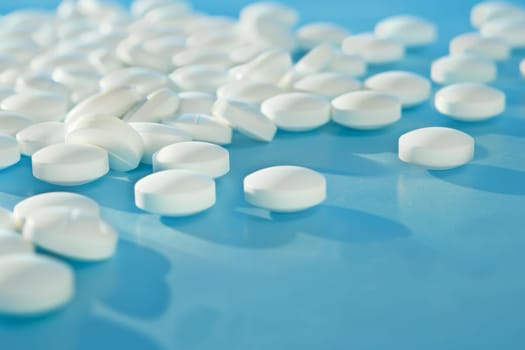 A blue table is covered with numerous white pills, creating a striking visual of medication spread out. The pills are neatly arranged in rows on the surface, presenting a clinical and organized appearance.