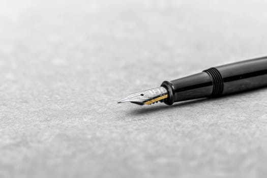 A fountain pen lays on top of a wooden table, its metallic nib gleaming under the light. The pen is surrounded by papers and notebooks, suggesting a writers workspace.
