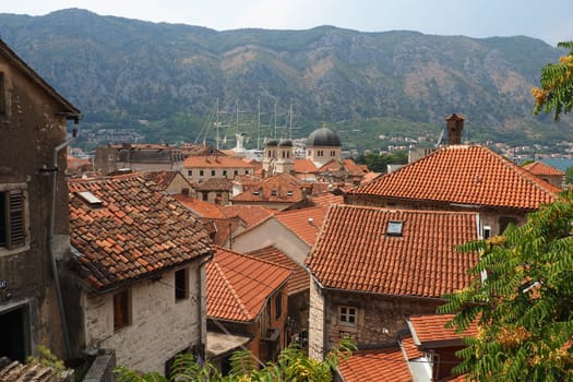 Kotor is a coastal city in Montenegro. Bay of Kotor. Red tiled roofs, mountain and chimneys of a tourist ship. Excursions and tourism. Cathedral of Saint Tryphon. Medieval old towns in the Adriatic.