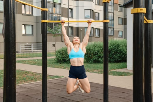Woman pulls herself up on bar on sports field of residential area