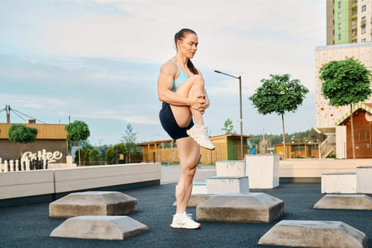 Low angle view at muscular woman stretching leg on sports ground of residential area