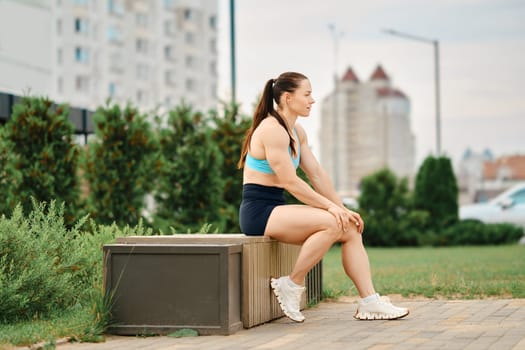 Woman bodybuilder resting while sitting on bench in backyard of residential area