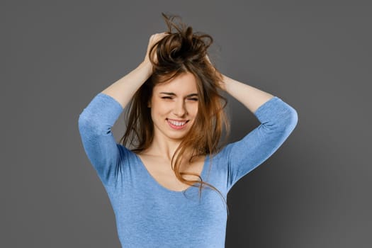 Young woman fooling around and mussing her hair with her hands over grey studio background