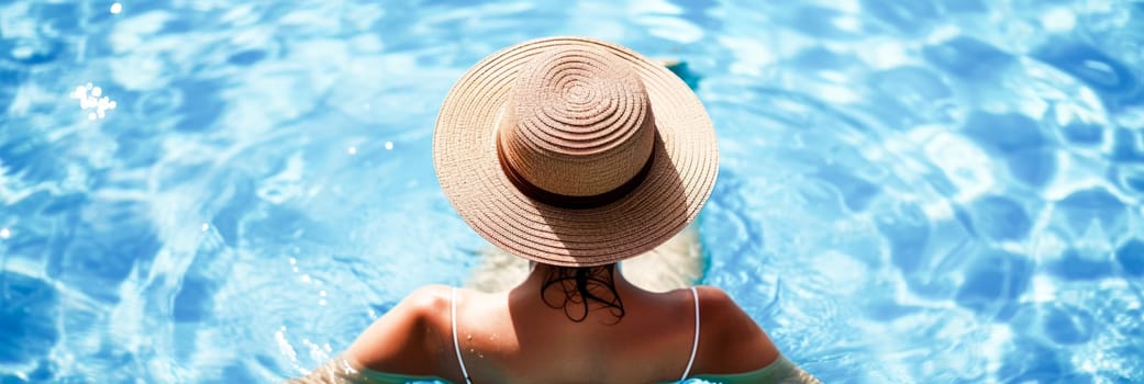 A woman enjoying the sun by the pool, seen from behind, with a straw hat. Focus on relaxation and leisure.Ideal for wide-format use with ample copy space.