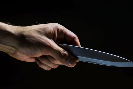 A person is shown holding a knife in their hand. The individuals grip is firm, and the blade is visible, pointing downwards. The background is neutral, emphasizing the action taking place.