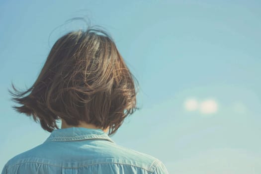 A person with long hair is standing confidently in front of a striking blue sky. The individual appears serene and composed against the vibrant backdrop of the clear sky.