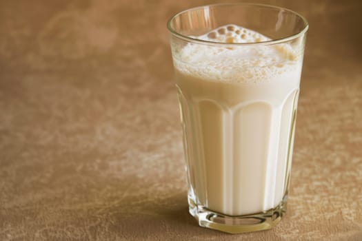 A tall glass filled with milk sits on a wooden table, reflecting the light from above. The glass is translucent, showcasing the white liquid inside. Its condensation marks the surface underneath.