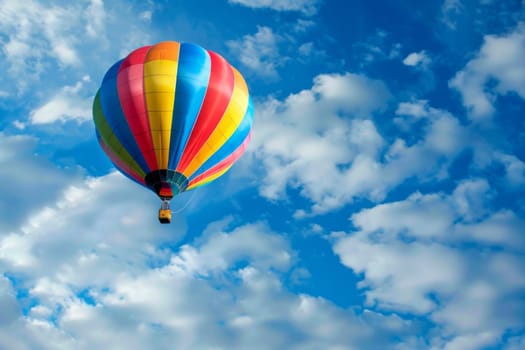 A vibrant hot air balloon, in various colors, soars majestically through a clear blue sky. The balloon is filled with hot air, propelling it upwards with passengers on board enjoying the aerial view.