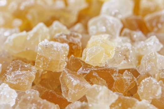 A mound of sugar crystals in shades of yellow and white is piled high, glistening under the light. The crystals are irregular in shape, reflecting the granulated texture of sugar.