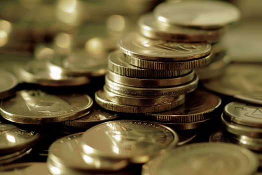 A collection of coins piled neatly on top of a wooden table. The coins appear to be a mix of different denominations and metals, reflecting a variety in value and currency. The table surface is smooth and highlights the shine and details of each coin.