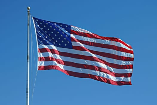 The American flag gracefully flutters in the wind, showcasing its red and white stripes and bright stars against a clear blue sky.