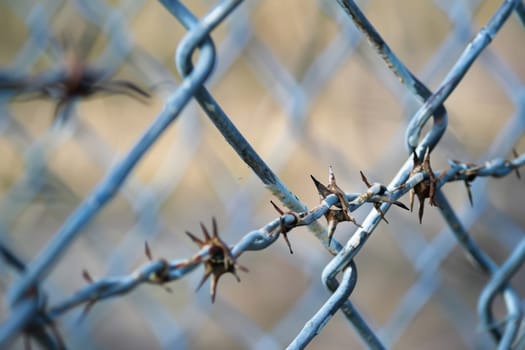 A close-up view of a silver chain link fence, showing its interlocking links and metal construction. The fence is weathered with rust spots and sits against a blurred background.