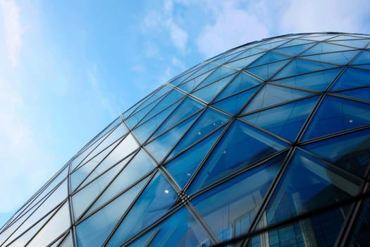 A tall and imposing glass building dominates the skyline against the backdrop of a clear blue sky. The reflective surfaces of the structure catch the sunlight, creating a striking visual contrast with the vast expanse of the sky.