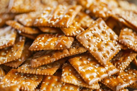 A substantial pile of sesame seed crackers stacked together, each cracker topped generously with sesame seeds. The golden-brown crackers are crispy and appear savory, with a sprinkling of small sesame seeds adding texture.