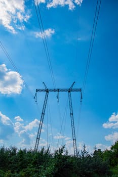 The towers of the power line of energy with cables against the background of nature. High -voltage tower of transmission of electric energy. Industry and nature. Blue sky with white clouds.