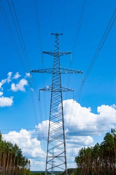 The towers of the power line of energy with cables against the background of nature. High -voltage tower of transmission of electric energy. Industry and nature. Blue sky with white clouds.