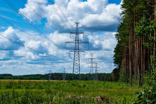 The towers of the power line of energy with cables against the background of nature. High -voltage tower of transmission of electric energy. Industry and nature. Blue sky with white clouds.
