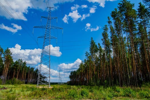 The towers of the power line of energy with cables against the background of nature. High -voltage tower of transmission of electric energy. Industry and nature. Blue sky with white clouds.