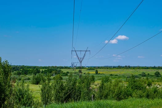 The towers of the power line of energy with cables against the background of nature. High -voltage tower of transmission of electric energy. Industry and nature. Blue sky with white clouds.