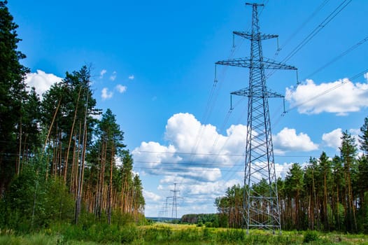 The towers of the power line of energy with cables against the background of nature. High -voltage tower of transmission of electric energy. Industry and nature. Blue sky with white clouds.