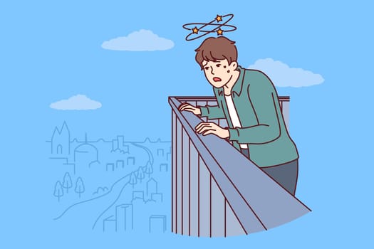 Frightened man with acrophobia and fear of heights looks down from roof of skyscraper trying to overcome fear. Guy with acrophobia syndrome feels dizzy when looking at city from above