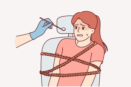 Woman is afraid of dentist and feels panic, sitting tied to chair for examining patients in dental clinic. Girl experiences dentaphobia, and fear of treating caries or visiting dentist