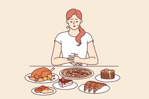 Problem of overeating in woman sitting at table with fast food, and in need of balanced diet. Girl feels heaviness in stomach due to regular overeating, which causes deterioration of immune system.