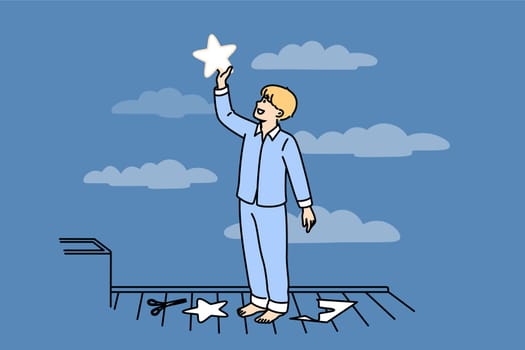 Little boy puts paper star to sky, thinking about endless space and galaxies, dressed in pajamas. Happy child dreams of seeing clean party welcome and wanting to fly into space when grows up