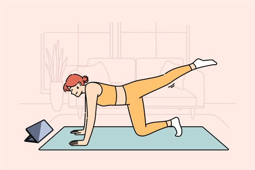 Woman doing fitness watching online lesson from trainer, doing stretching on sports mat in living room. Girl is interested in fitness and health-improving gymnastics, thanks to webinars from internet.