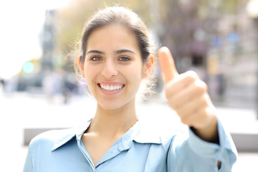 Happy woman gesturing thumbs up at camera in the street