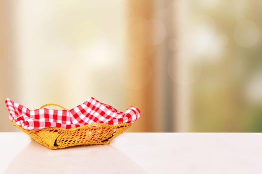 Empty picnic basket. Close-up of a empty straw basket with a checkered red napkin on table over blurred kitchen background. For food and product display montage.