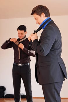 Two men in suits tie their ties