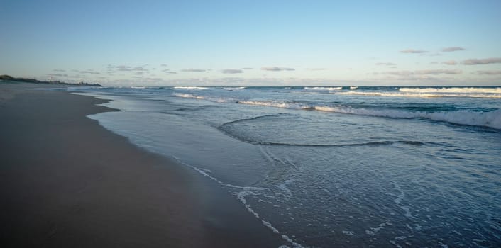 Sunshine Coast, Warana, Kawana showing a beach scene in the late afternoon with dark blue water, white surf waves, wet sand on the shoreline and the setting sun still shining on some of the ocean.