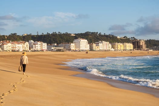 Nazaré, Portugal - Mars 19 2024: Woman walking on the Nazaré Beach and the Atlantic Ocean, Portugal