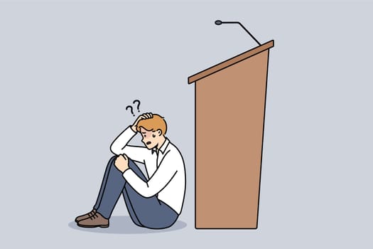 Man experiences peiraphobia, which causes fear speaking in front of audience, and sits near empty podium with microphone. Problem peiraphobia in person with no experience in conducting business events