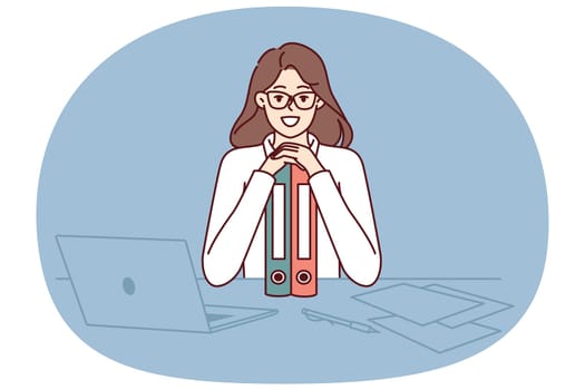 Business woman sits at table leaning on folders and smiling looking at camera rejoicing at success in career as office clerk. Girl manager with documents on desk rejoices at end of business audit