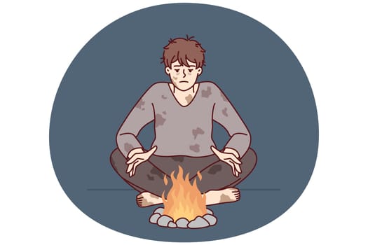 Homeless man in dirty clothes warms hands sitting by fire trying to survive due to lack of own home. Homeless guy needs help from social services and benefits or food stamps after losing job