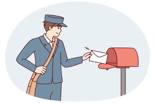 Man in postman uniform throws paper letter into metal mailbox located on street. Guy delivers fresh mail with alerts from government agencies or messages from friends