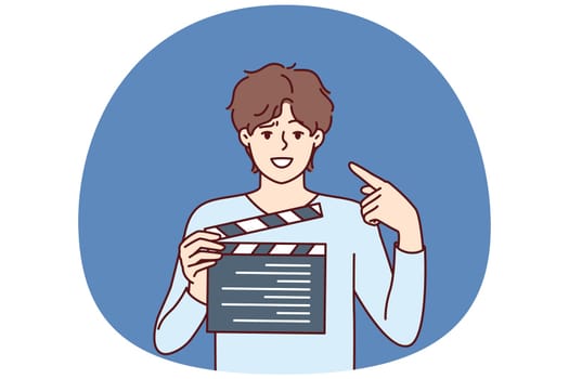 Man producer with clapboard in hands looks at screen while working on set of film or clip with Hollywood actors. Guy director or producer points finger at face, recommending staff of set to smile