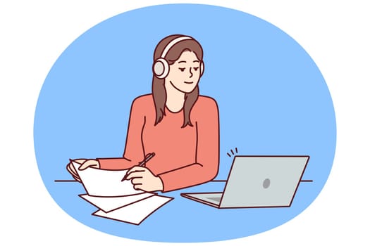 Woman with laptop sits at table and watches training webinar for gaining new skills and makes notes on paper. Attentive girl in headphones using laptop to get online education at university or college