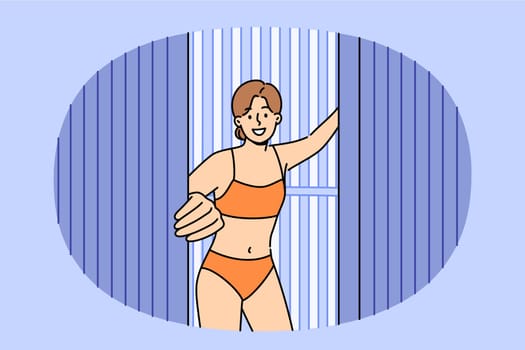 Woman comes out of vertical solarium, urging people to stop sunbathing, which causes skin cancer due to ultraviolet light. Girl visitor solarium stands in swimsuit, enjoying visit SPA treatments