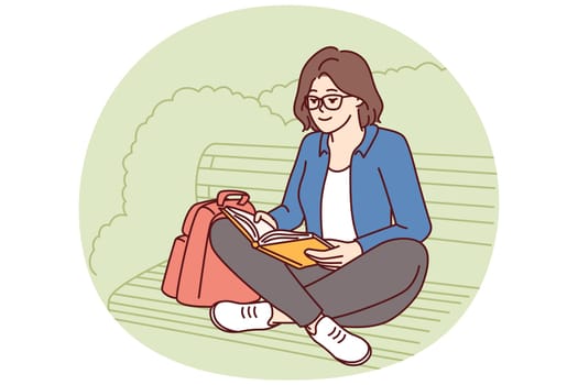 Teenage girl is reading book sitting on park bench enjoying good summer weather and intriguing plot of novel or fiction. Young woman spends leisure time outdoors doing self-education