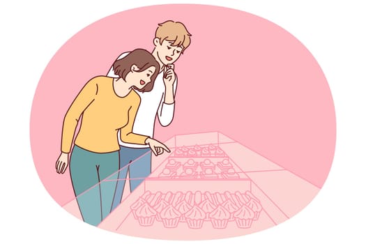 Young couple stands near showcase of pastry shop with cakes and desserts under transparent glass. Guy and girl went to cafeteria to have breakfast and choose cupcakes or donuts to satisfy hunger
