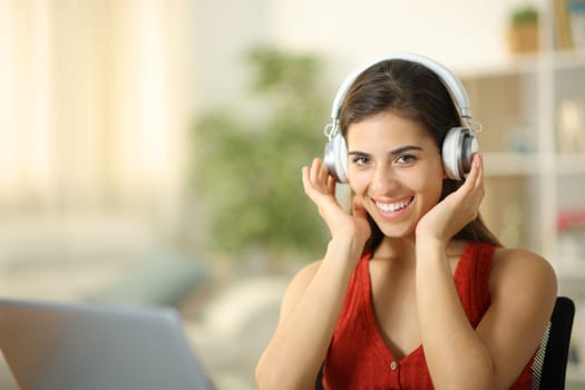 Happy woman wearing headphone looks at camera sitting at home