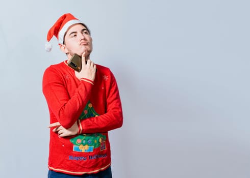 Thoughtful man with christmas hat holding cell phone, Young man in christmas clothes thoughtful with cell phone isolated, Handsome man in christmas clothes thoughtful holding cell phone