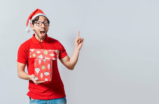Christmas man with surprised face holding a gift pointing up. Amazed christmas man holding gifts pointing up. Surprised christmas man holding gifts and pointing up. Christmas man pointing a promo