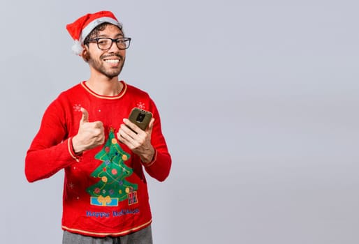 Smiling guy in christmas hat using cellphone with thumb up. Smiling young man in christmas hat using cellphone and giving thumbs up. People in santa hat using phone and doing ok gesture