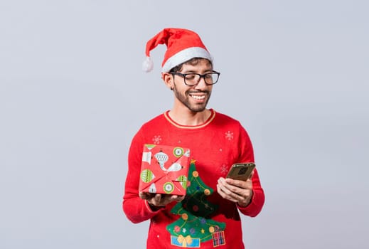 Christmas man holding gift box and telephone isolated. Handsome man in christmas hat holding gift and looking at phone, Guy in christmas hat holding gift box and smiling at smartphone